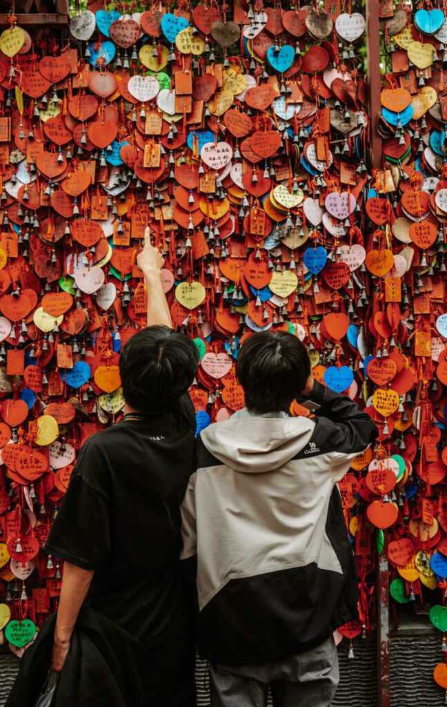 Two boys standing in front of a wall of hanging heart love notes.