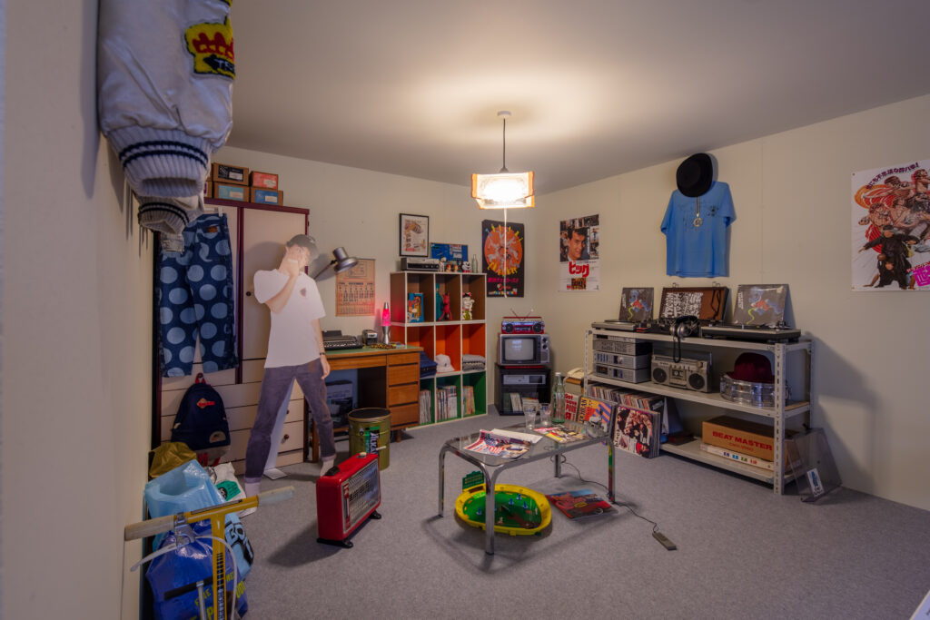 Inside teenage Nigo's 1980s bedroom. It features a life-size cutout of young NIGO (Tomoaki Nagao) alongside collectables that reveal his early affinity for American pop culture.