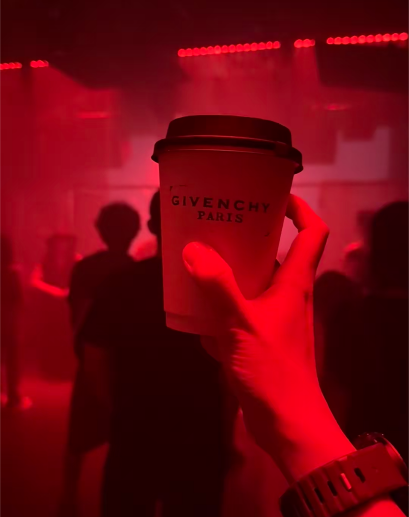 A clubber holding a cup of Givenchy-branded soy milk on the red-lit dance floor at Aby'ss club during the 2026 Shanghai 'Givenchy Breakfast' pop-up.