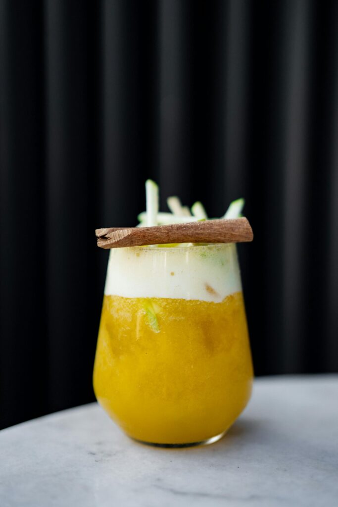 Glass of fizzy jamu garnished with cinnamon stick